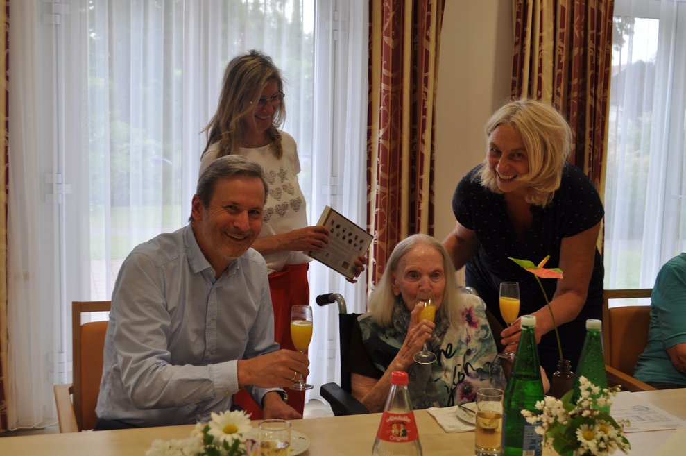 einige Menschen bei einer Geburtstagsfeier mit Blumen, Sekt und Pralinen
