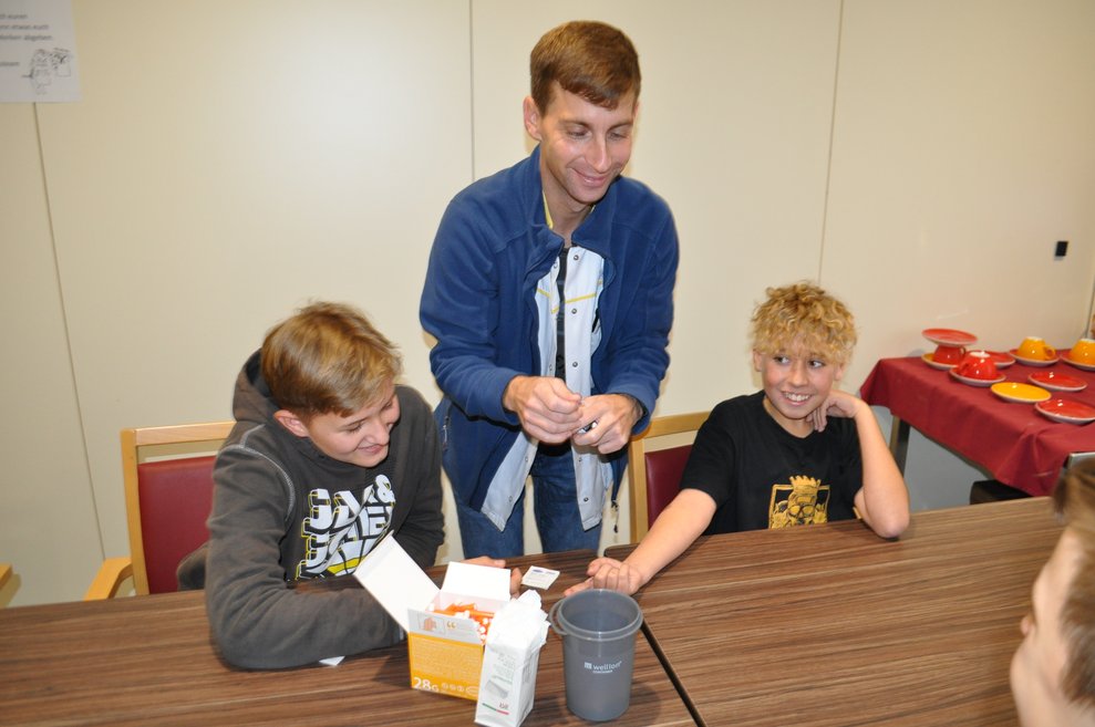 ein Mann zeigt zwei Buben wie man Blutzucker misst