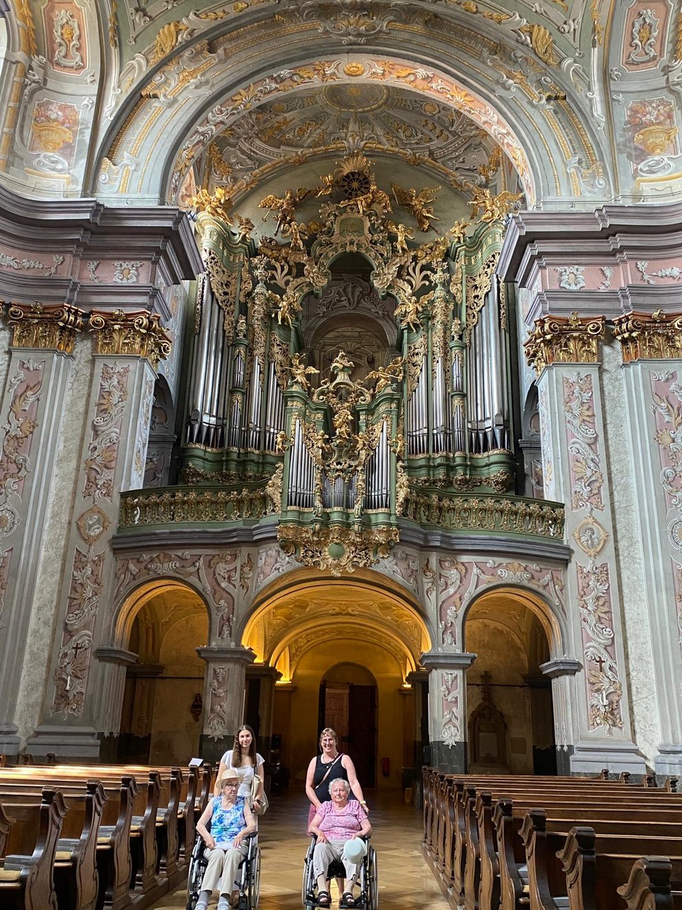 Zwei ältere Damen im Rollstuhl mit Begleitpersonen in einer Kirche