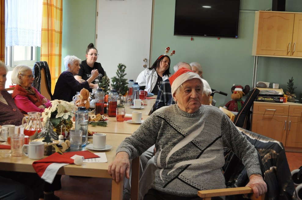 einige ältere Menschen mit Weihnachtsmann Mützen und weihnachtlich gedeckten Tischen