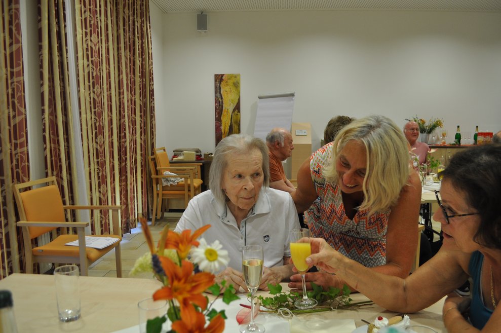 einige Menschen bei einer Geburtstagsfeier mit Blumen, Sekt und Pralinen