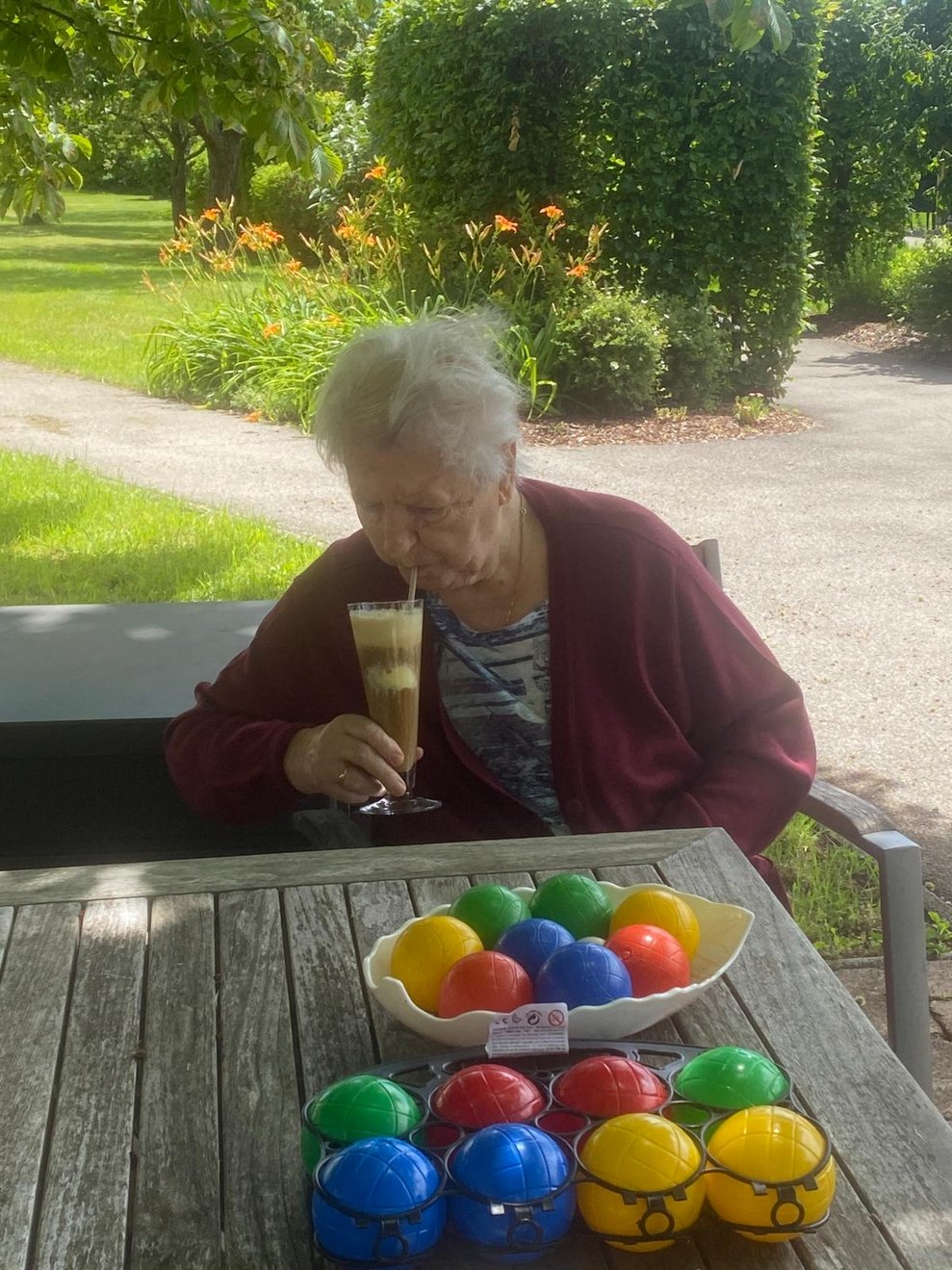 eine ältere Dame trinkt im Garten einen Eiskaffee