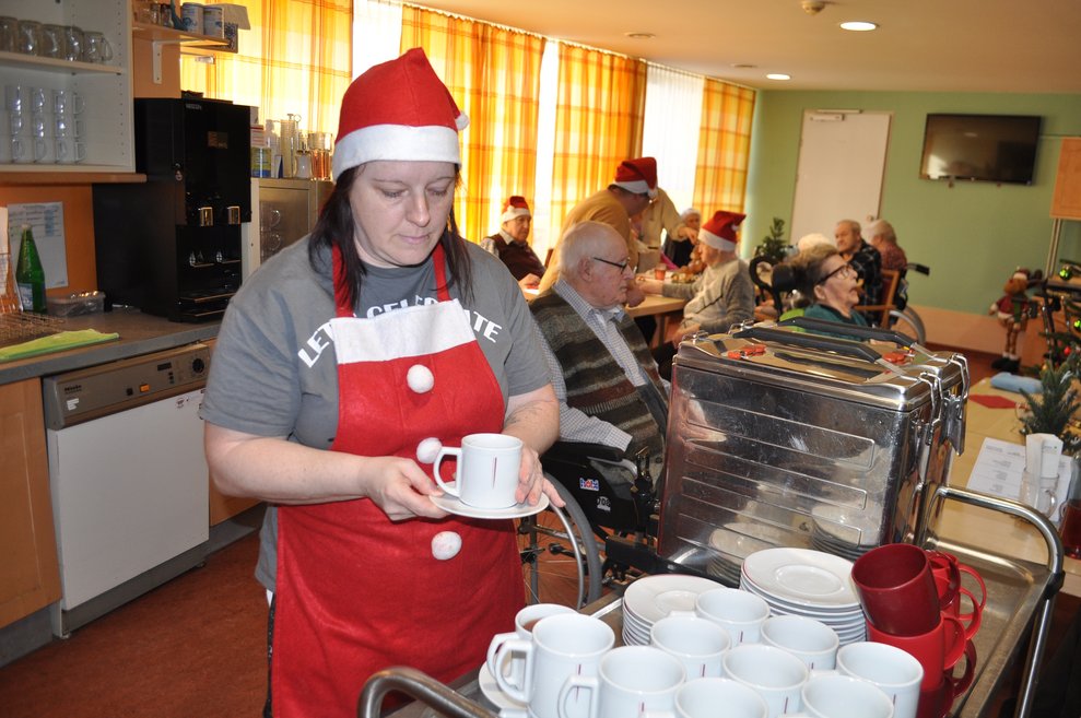 eine Mitarbeiterin als Weihnachtsmann verkleidet schenkt Tee und Punsch aus