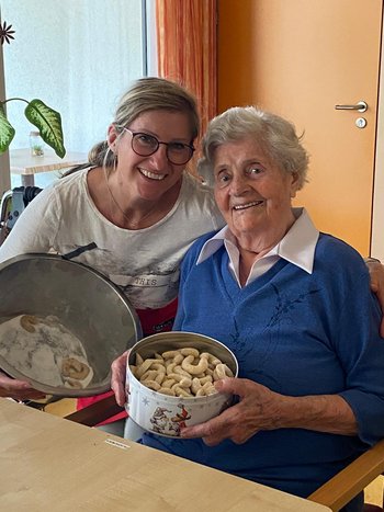 eine ältere Dame und eine jüngere mit zwei Keksdosen 