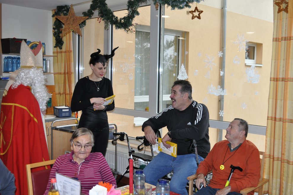 eine Frau als Krampus verkleidet und ein Mann als Nikolaus verkleidet bei zwei Männern und einer Dame zu Besuch im Pflegeheim
