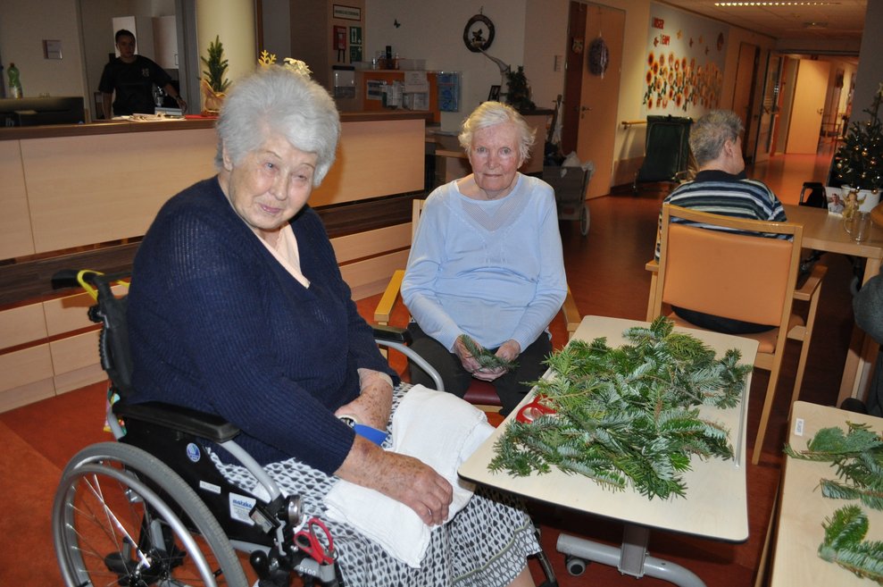 Zwei ältere Damen mit Tannenzweigen beim Adventkranzbinden