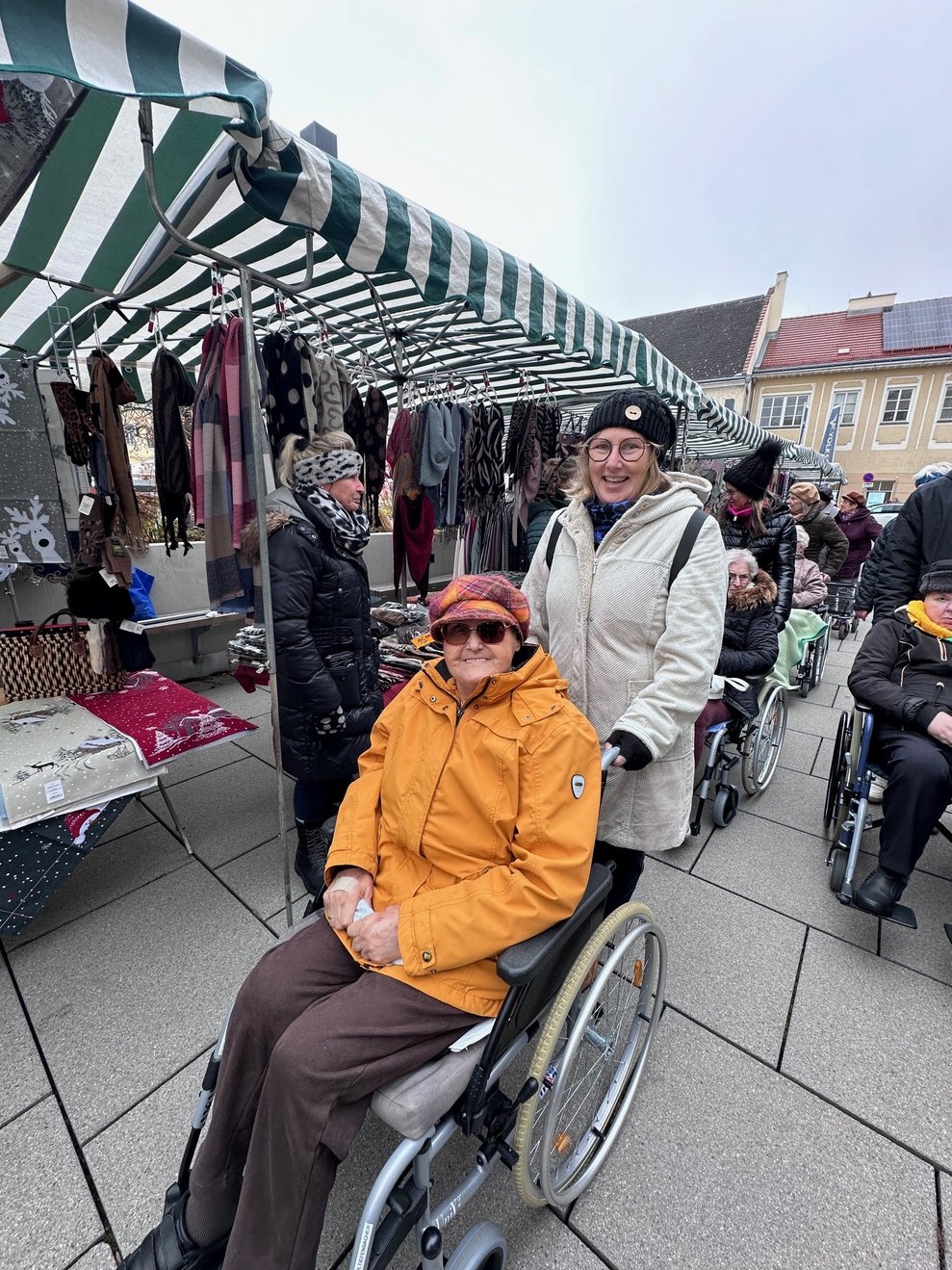 eine Dame im Rollstuhl mit einer Begleitperson am Markt