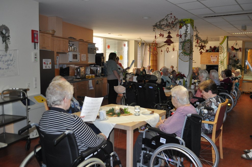 einige ältere Menschen bei weihnachtlich gedeckten Tischen und singen Weihnachtslieder