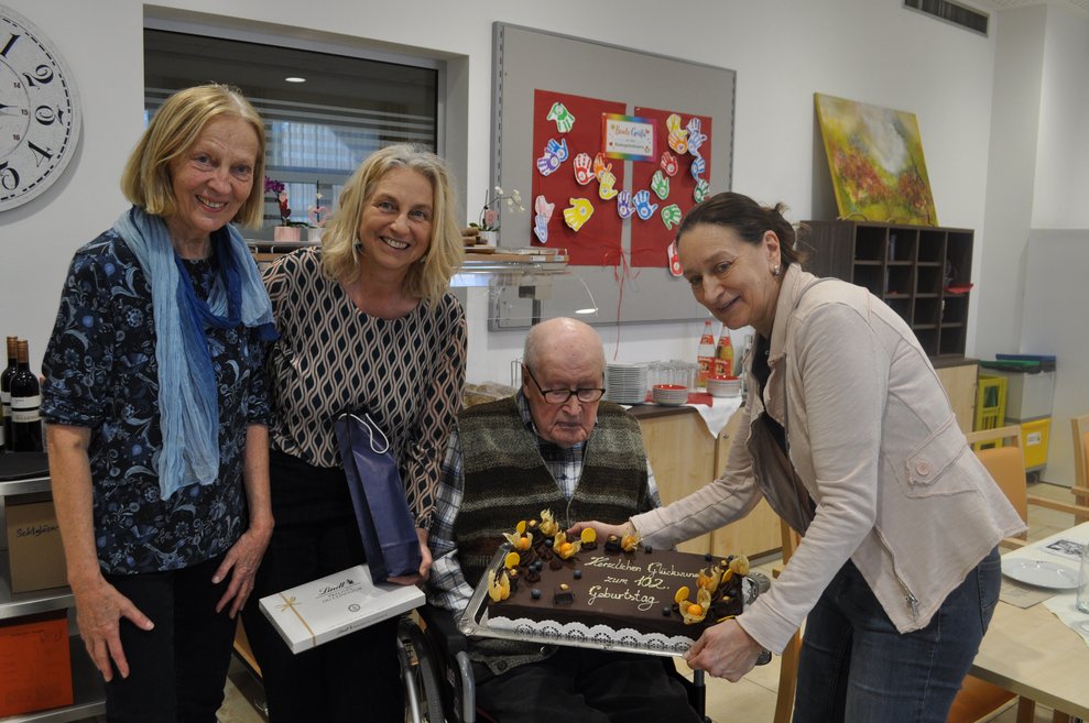 drei Damen mit dem Geburtstagskind - ein älterer Herr im Rollstuhl mit der Torte zum 102.- Geburtstag