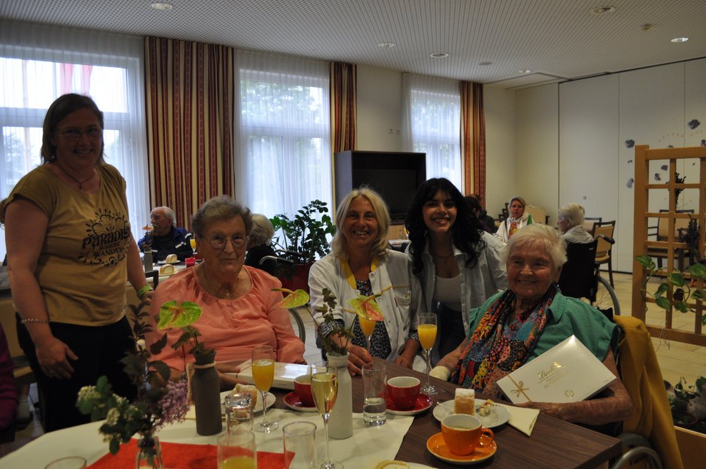 einige Menschen bei einer Geburtstagsfeier mit Blumen, Sekt und Pralinen