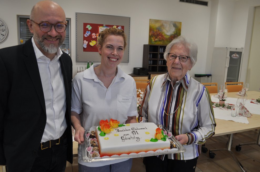 ein Mann, eine Frau und eine ältere Frau mit Geburtstagstorte