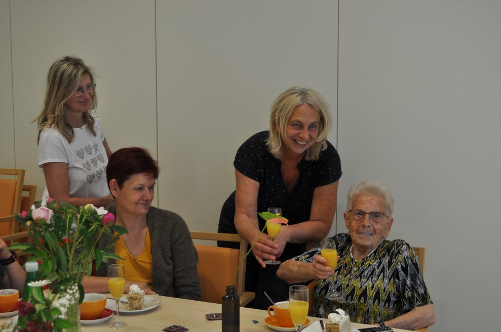 einige Menschen bei einer Geburtstagsfeier mit Blumen, Sekt und Pralinen