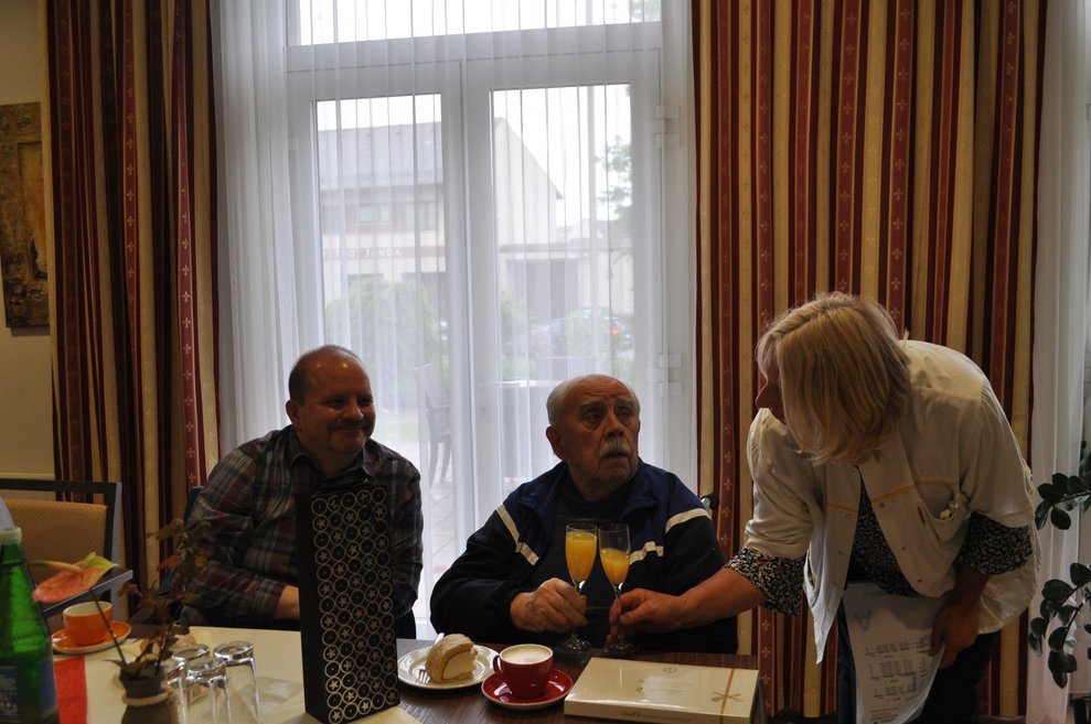 einige Menschen bei einer Geburtstagsfeier mit Blumen, Sekt und Pralinen