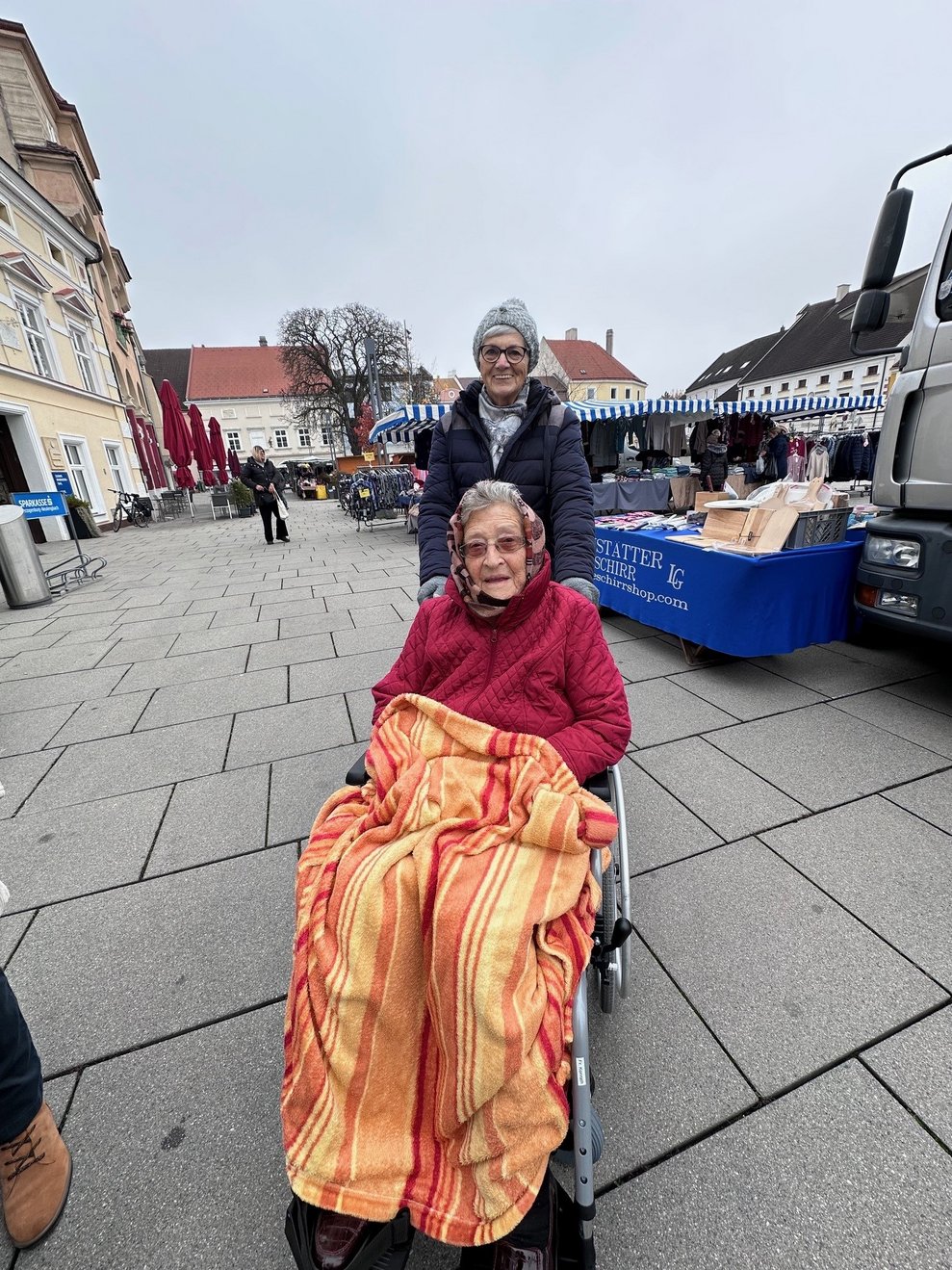 eine Dame im Rollstuhl mit einer Begleitperson am Markt